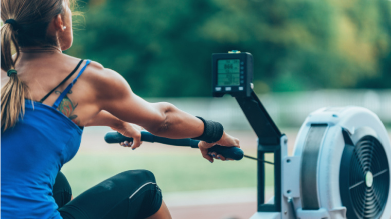 Long-haired person using rowing machine outdoors