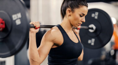 Long-haired person in gym doing barbell squat