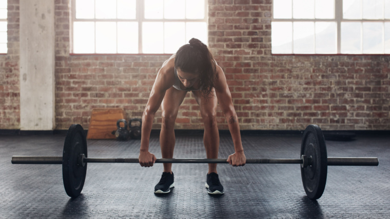 Long-haired person in gym preparing to lift barbell off ground